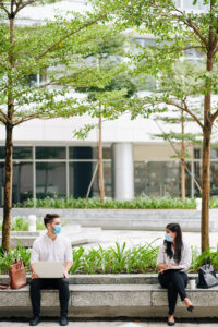 A man and a woman wearing masks sitting far apart from each other while working outside.