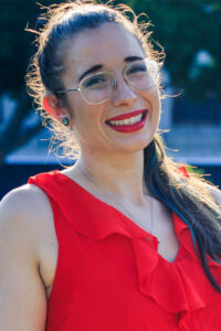 Katherine McDonald smiling wearing glasses and red lipstick.